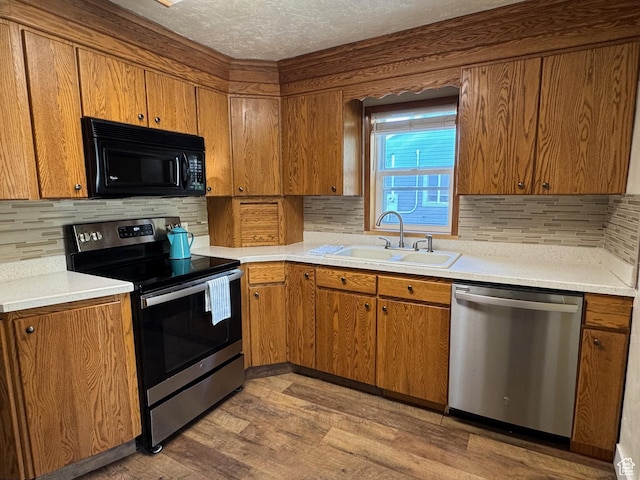 kitchen with brown cabinetry, a sink, light wood-style flooring, and stainless steel appliances