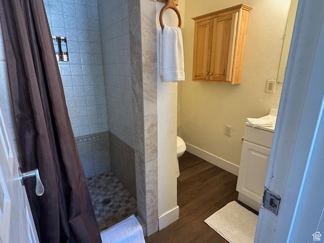 full bath featuring a tile shower, wood finished floors, vanity, baseboards, and toilet