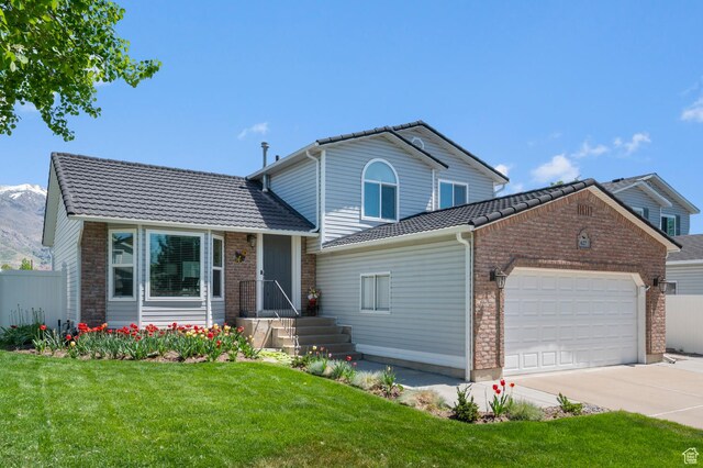 split level home featuring brick siding, a garage, a front lawn, and driveway