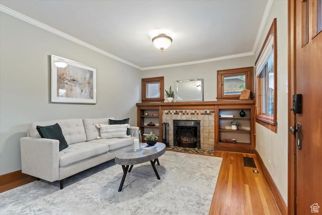 living area featuring light wood finished floors, a tiled fireplace, baseboards, visible vents, and ornamental molding
