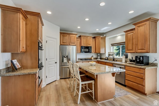 3381 W Slate View Dr, South Jordan, UT 84095 - kitchen with a breakfast bar area, a sink, light stone counters, black appliances, and light wood finished floors