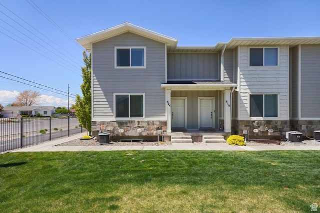 view of front of house featuring fence, a front yard, stone siding, board and batten siding, and central air condition unit