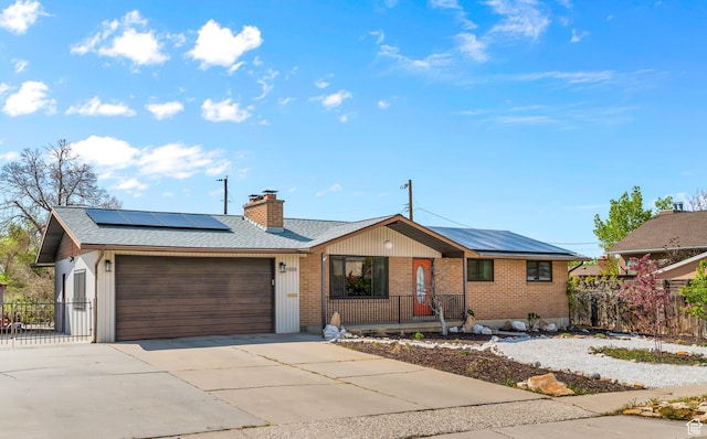 ranch-style home with driveway, a chimney, roof mounted solar panels, and a garage