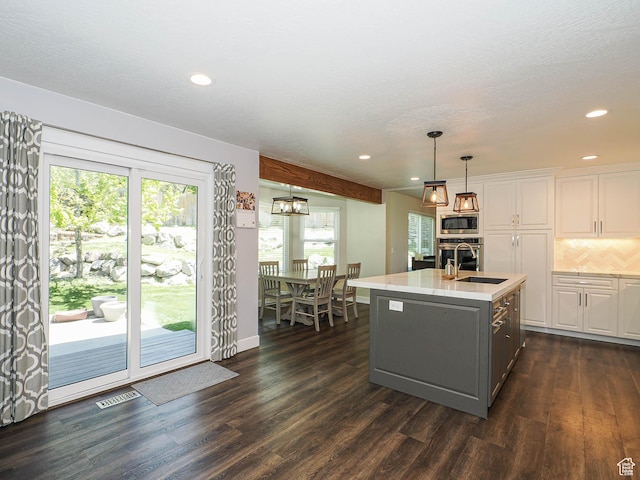 kitchen with a sink, white cabinets, dark wood-type flooring, stainless steel appliances, and an island with sink