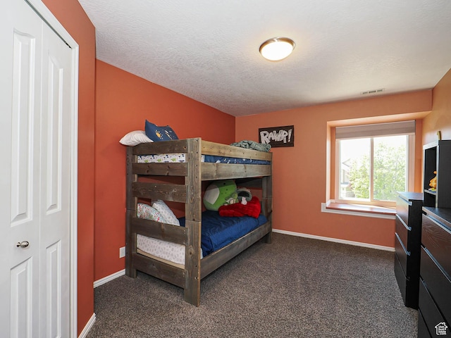 bedroom with a textured ceiling, baseboards, visible vents, and dark carpet