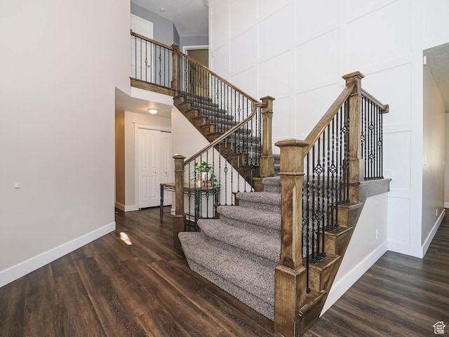 staircase featuring baseboards, wood finished floors, and a towering ceiling