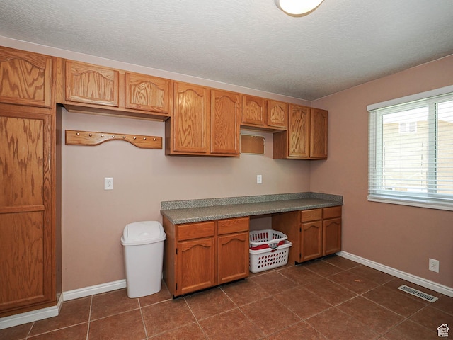 kitchen featuring a textured ceiling, brown cabinetry, baseboards, dark tile patterned floors, and visible vents