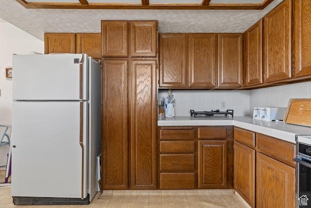375 Hillcrest, Central, UT 84722 - kitchen featuring freestanding refrigerator, brown cabinets, tile countertops, and tasteful backsplash