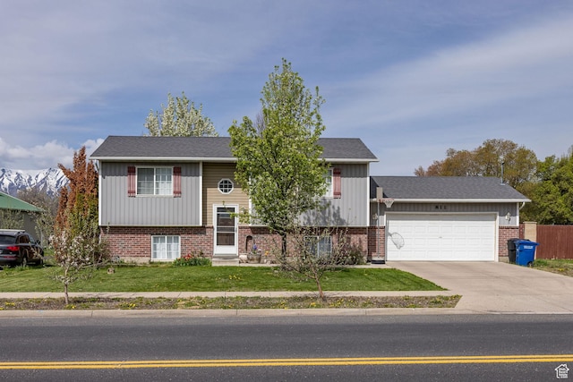 bi-level home with driveway, brick siding, fence, a front lawn, and an attached garage
