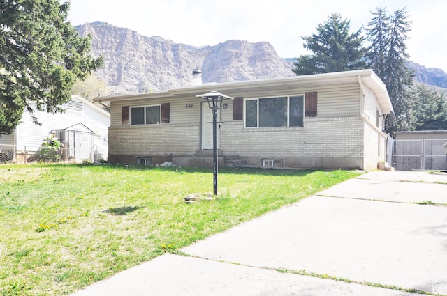 view of front facade featuring brick siding, an outdoor structure, a mountain view, a storage unit, and a front lawn