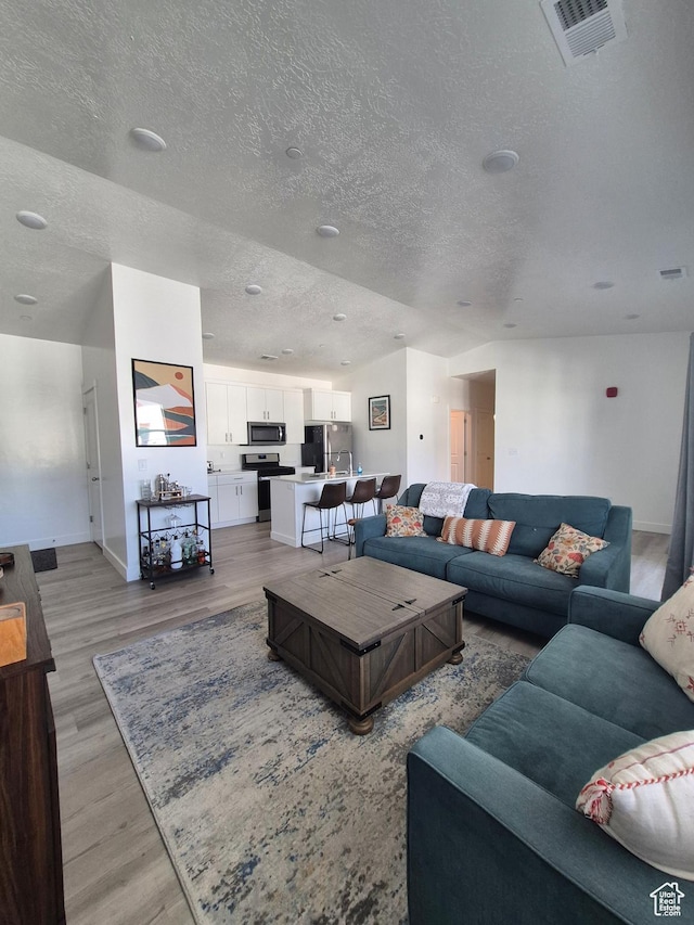 living room featuring baseboards, light wood finished floors, a textured ceiling, and visible vents
