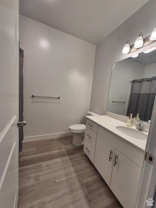 full bathroom with vanity, toilet, a textured ceiling, baseboards, and wood finished floors