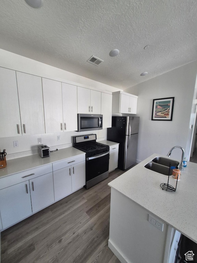 kitchen with dark wood-style flooring, visible vents, appliances with stainless steel finishes, a sink, and white cabinets