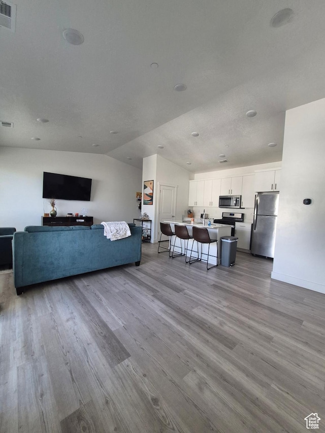 living area with baseboards, visible vents, wood finished floors, and lofted ceiling