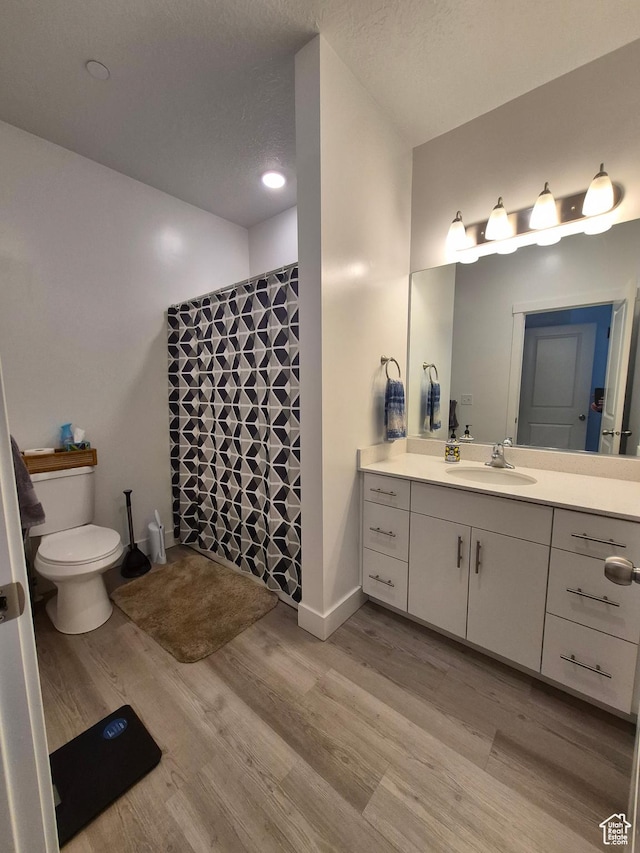 full bath with wood finished floors, baseboards, vanity, toilet, and tiled shower
