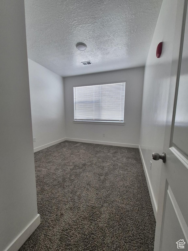 spare room with visible vents, a textured ceiling, dark carpet, and baseboards