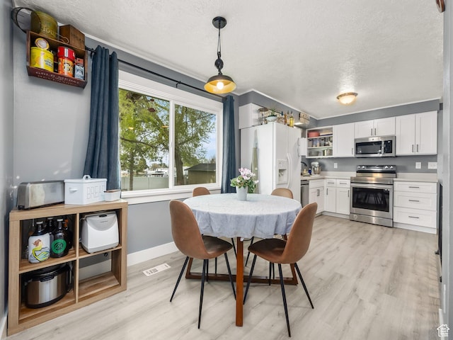 dining area featuring visible vents, light wood-style flooring, a textured ceiling, and baseboards
