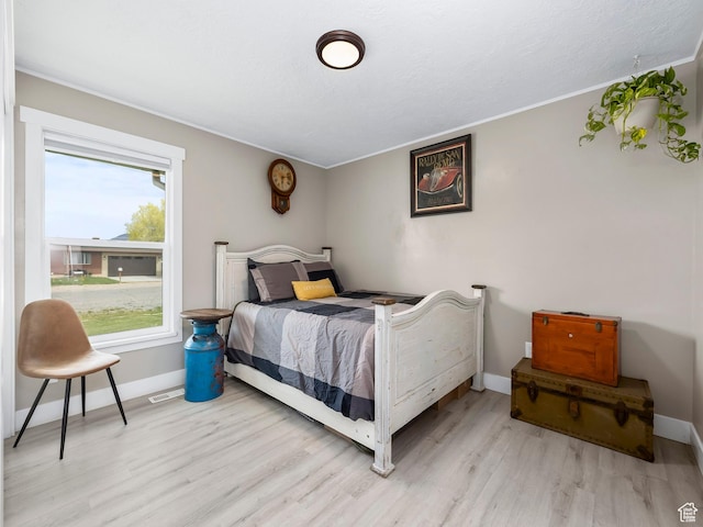 bedroom featuring baseboards, ornamental molding, light wood finished floors, and visible vents