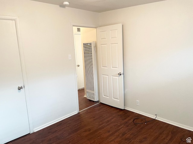 unfurnished bedroom with baseboards, a heating unit, and wood finished floors