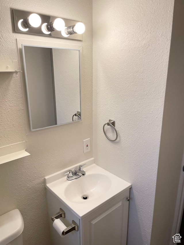 half bathroom featuring vanity, a textured wall, and toilet