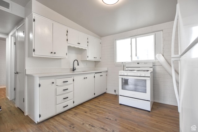 kitchen featuring visible vents, wood finished floors, a sink, white cabinets, and white appliances