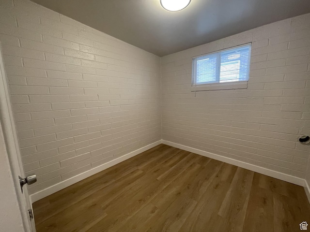 spare room featuring baseboards, dark wood-style flooring, and brick wall