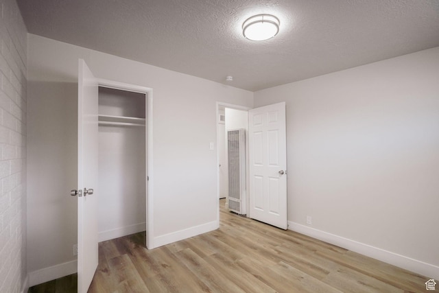 unfurnished bedroom featuring baseboards, a closet, light wood finished floors, and a heating unit