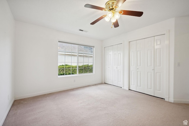 unfurnished bedroom with a ceiling fan, light colored carpet, visible vents, baseboards, and two closets