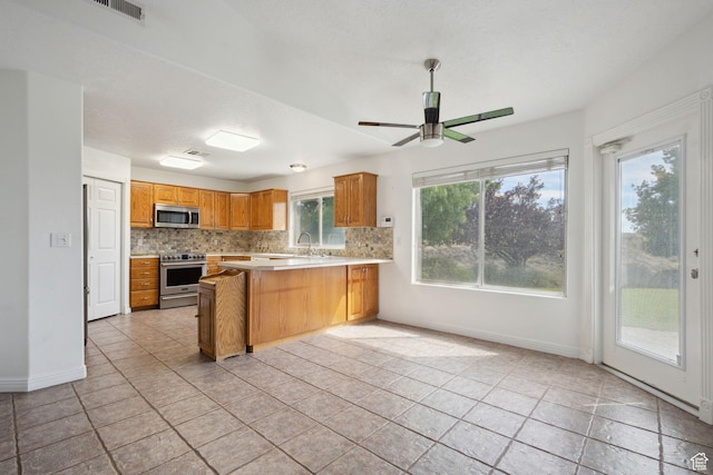 kitchen featuring appliances with stainless steel finishes, light countertops, a peninsula, baseboards, and backsplash