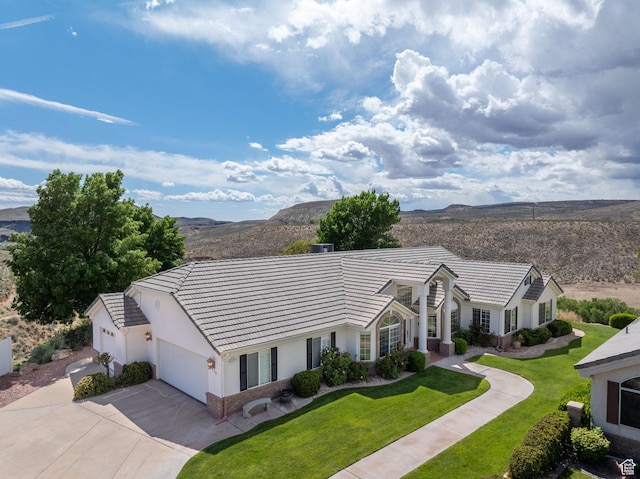ranch-style house featuring a front lawn, stucco siding, a mountain view, driveway, and a tile roof