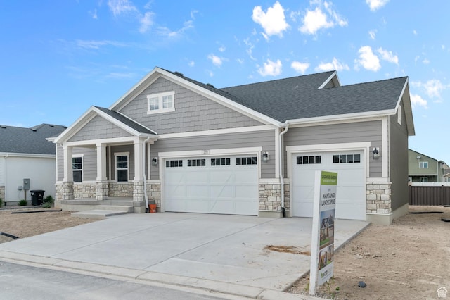 craftsman house with stone siding, a garage, concrete driveway, and covered porch