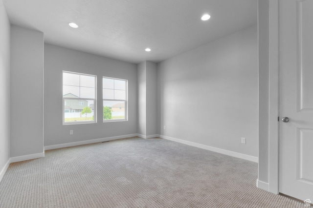 empty room featuring light carpet, recessed lighting, and baseboards