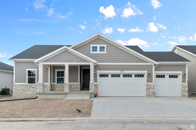 craftsman inspired home featuring a garage, stone siding, a porch, driveway, and cooling unit