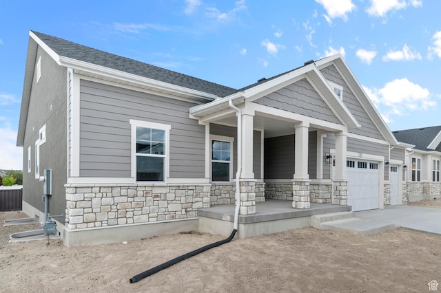 craftsman-style home featuring covered porch, stone siding, concrete driveway, and an attached garage
