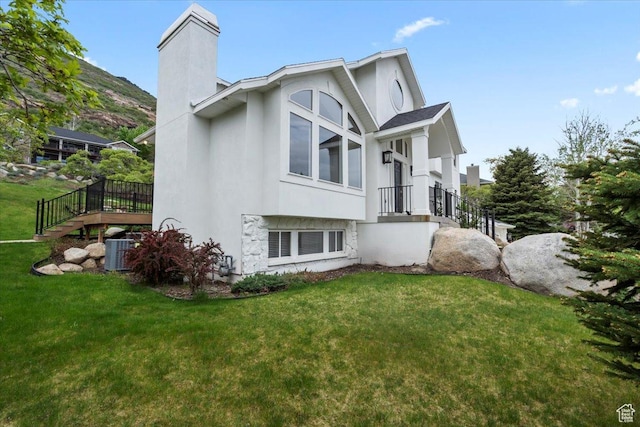 view of side of property featuring a chimney, a lawn, central AC, stucco siding, and stairway