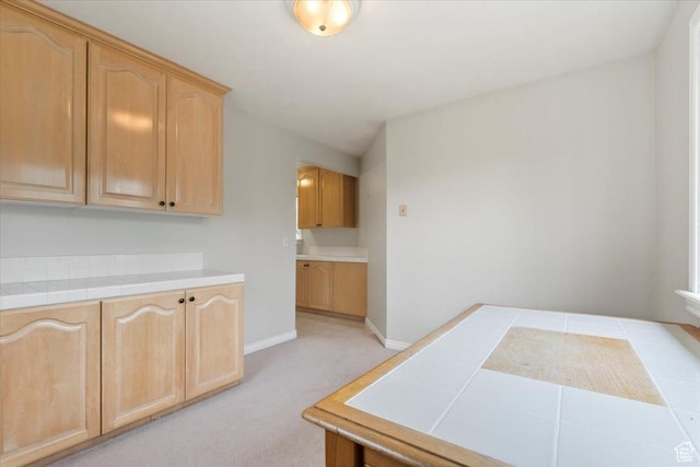 kitchen featuring baseboards, light carpet, light brown cabinets, and tile countertops