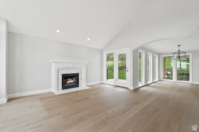unfurnished living room with light wood-type flooring, a chandelier, baseboards, and a high end fireplace