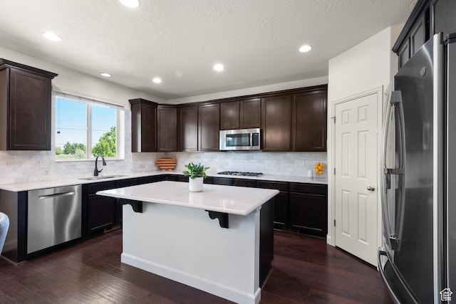 kitchen with dark brown cabinets, dark wood-type flooring, a center island, a sink, and stainless steel appliances