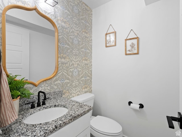 bathroom with vanity, an accent wall, toilet, baseboards, and wallpapered walls