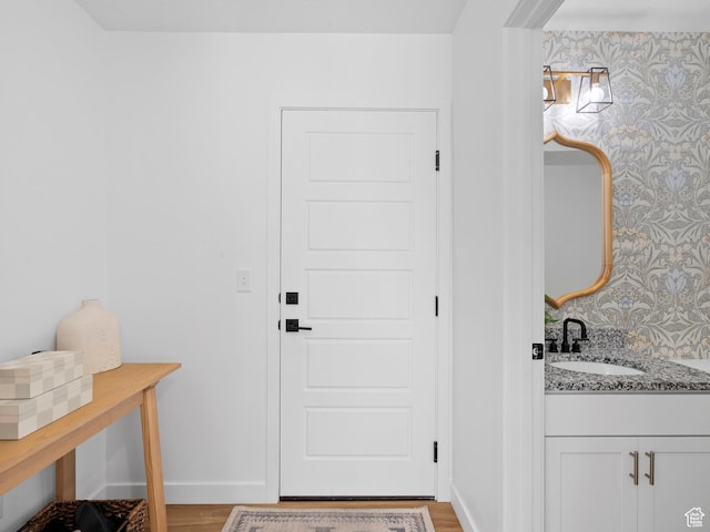 doorway to outside featuring baseboards, a sink, light wood-style flooring, and wallpapered walls