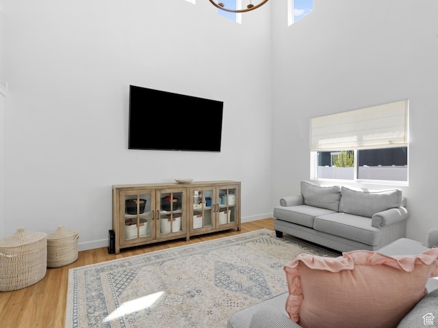 living area featuring baseboards, a chandelier, wood finished floors, and a towering ceiling