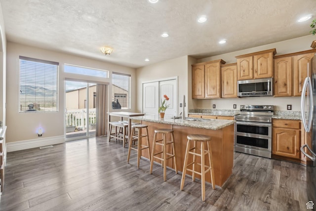 3214 W Ridgeline Rd, Stockton, UT 84071 - kitchen featuring a sink, a textured ceiling, an island with sink, stainless steel appliances, and a kitchen bar