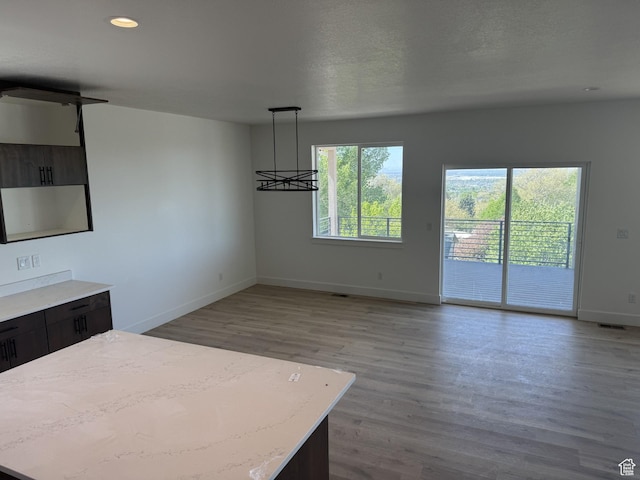 interior space with wood finished floors, a kitchen island, baseboards, open floor plan, and decorative light fixtures