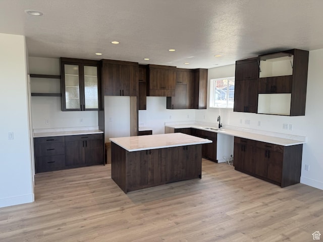 kitchen with open shelves, dark brown cabinetry, a sink, baseboards, and a kitchen island