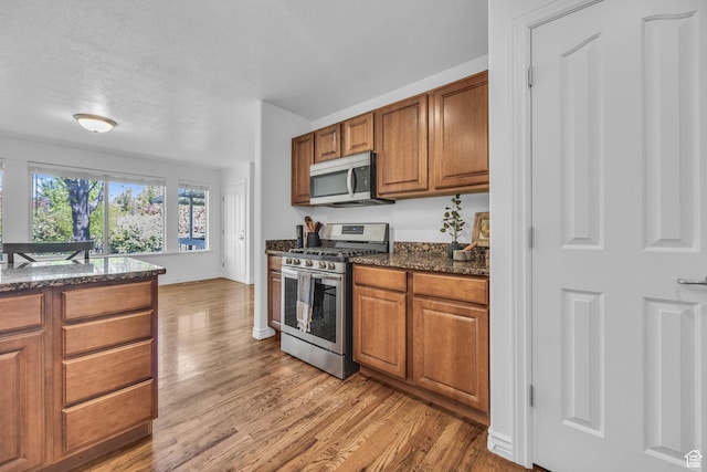 2948 W 150 N, Layton, UT 84041 - kitchen with stainless steel appliances, brown cabinets, light wood finished floors, dark stone counters, and a textured ceiling