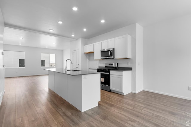1914 E Thunder Ln N Unit 505, Eagle Mountain, UT 84005 - kitchen with dark countertops, appliances with stainless steel finishes, a sink, open floor plan, and light wood-type flooring