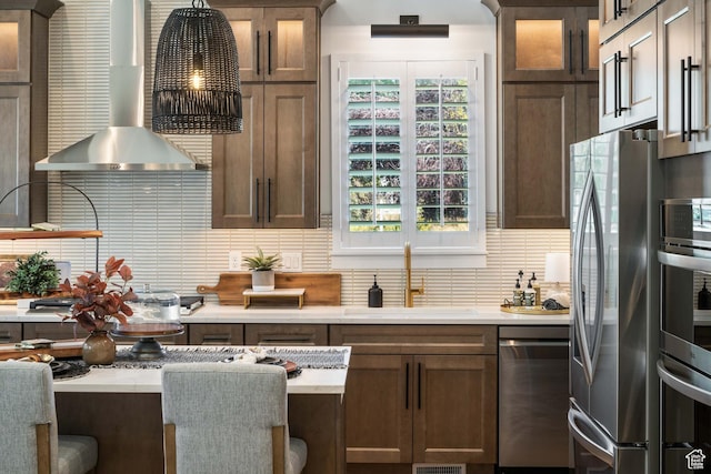 kitchen featuring wall chimney range hood, backsplash, appliances with stainless steel finishes, and a sink