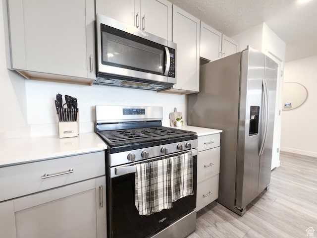 kitchen with gray cabinets, appliances with stainless steel finishes, light countertops, baseboards, and light wood finished floors