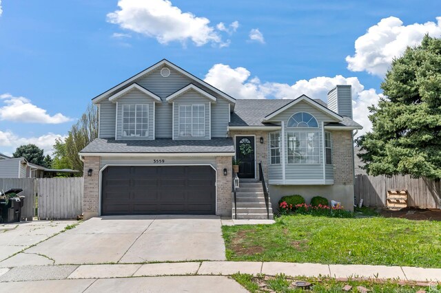 tri-level home featuring a garage, a front lawn, fence, brick siding, and driveway