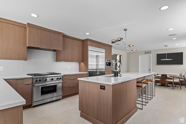 kitchen featuring high quality appliances, hanging light fixtures, a breakfast bar, a sink, and light countertops